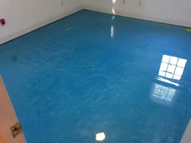 Blue, glossy epoxy floor in a room with white walls. Window reflects light.
