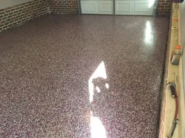 Garage floor with a speckled, maroon-colored epoxy coating. A garage door is in the background.