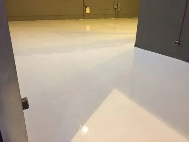 White epoxy-coated floor in an interior space, reflecting light with a slight sheen.