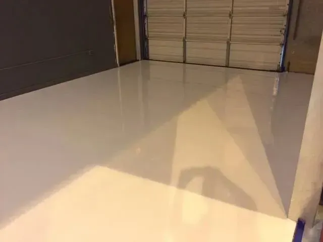 A garage interior with a glossy, white-painted floor. Gray wall on the left, garage door in the back.