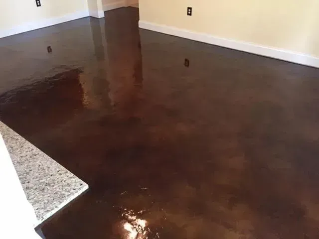 Brown stained concrete floor, reflecting light, in an empty room with white baseboards and light-colored walls.