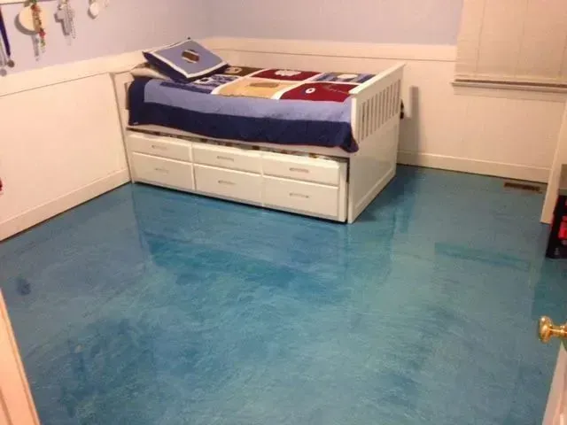 Bedroom with a blue metallic-effect floor, white bed with drawers, and blue bedding.