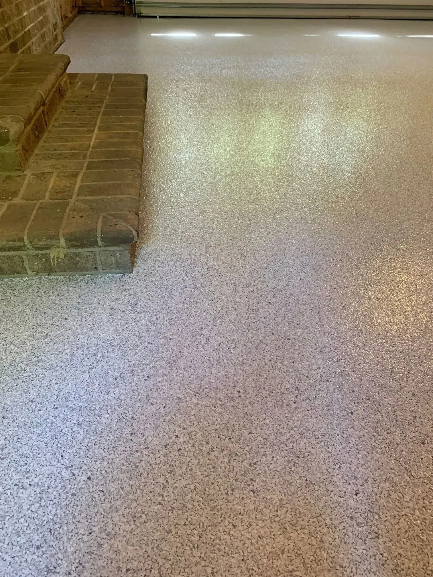 Epoxy-coated garage floor with speckles, beside brick steps, lit by sunlight, reflecting light.