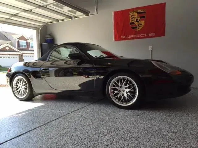 Black Porsche Boxster convertible in a garage with a red Porsche flag.