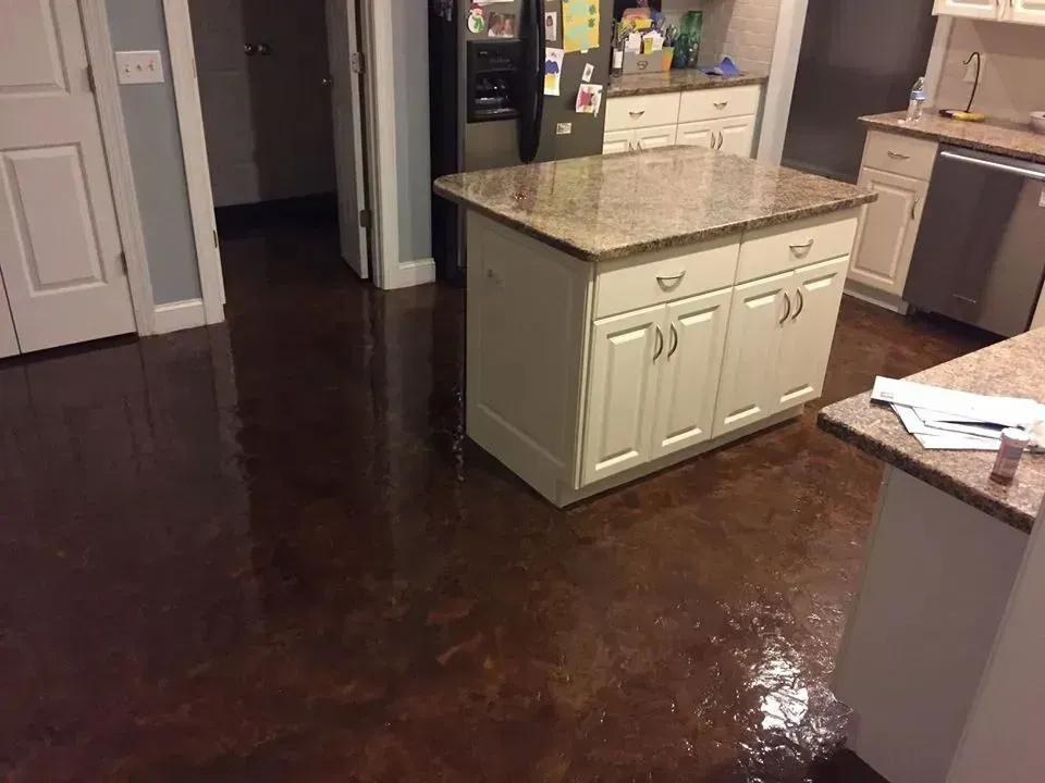 Brown stained concrete kitchen floor with an island, cabinets and appliances.