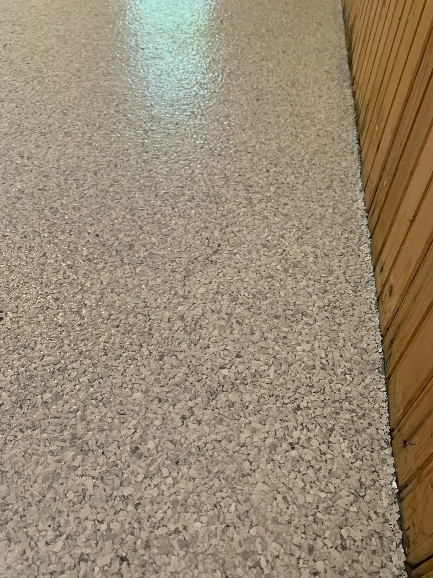 Light gray speckled flooring next to wood paneling.