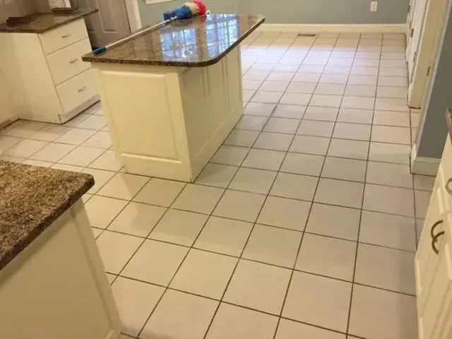 Kitchen with white tile floor, white cabinets, and a granite countertop island. A mop is resting on the island.