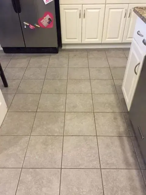 Gray tiled kitchen floor with white cabinets and a stainless steel refrigerator.