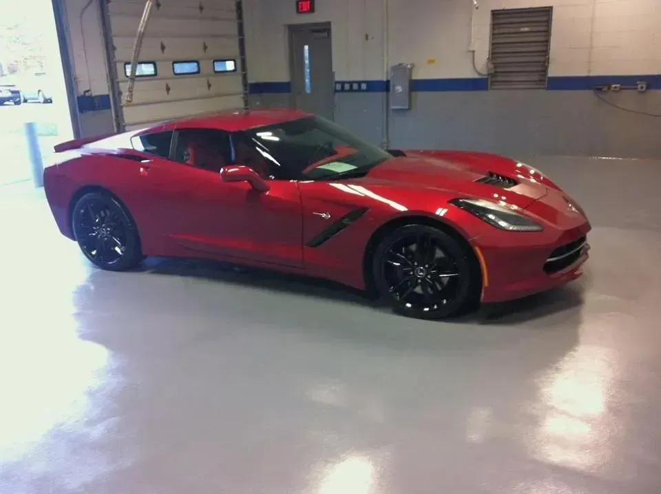 Red Corvette sports car parked in a garage with a gray floor and open door.