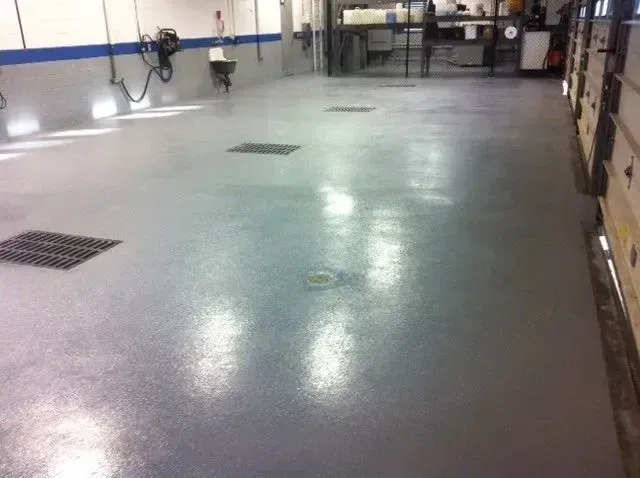 Gray concrete floor in a garage with four floor drains and a blue and gray painted wall.