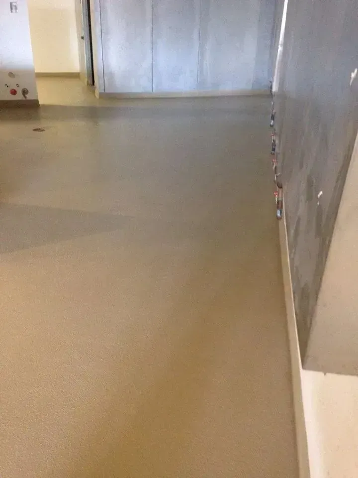 Light brown, smooth, concrete floor in a room with gray and white walls and an open doorway.