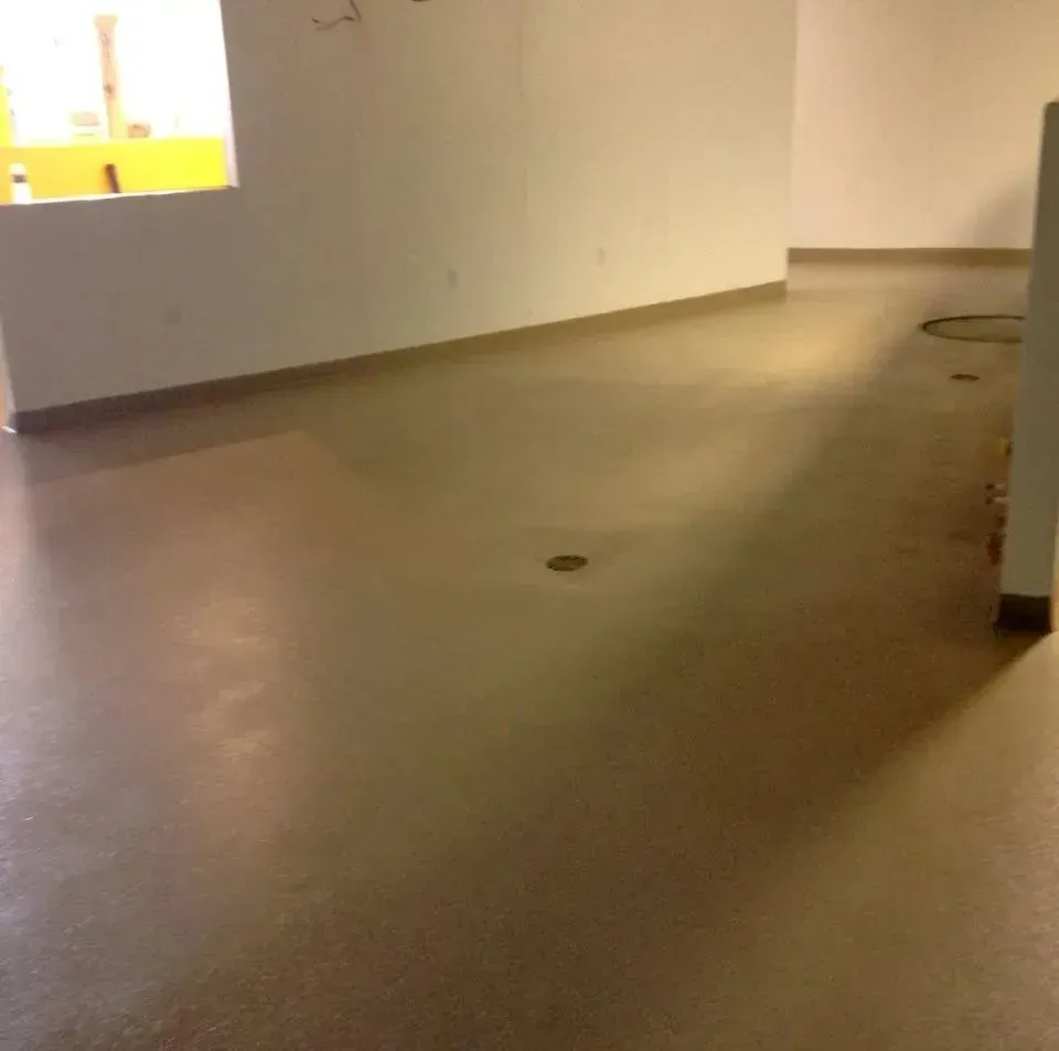 Empty office space with polished concrete floor, white walls, and a small window.