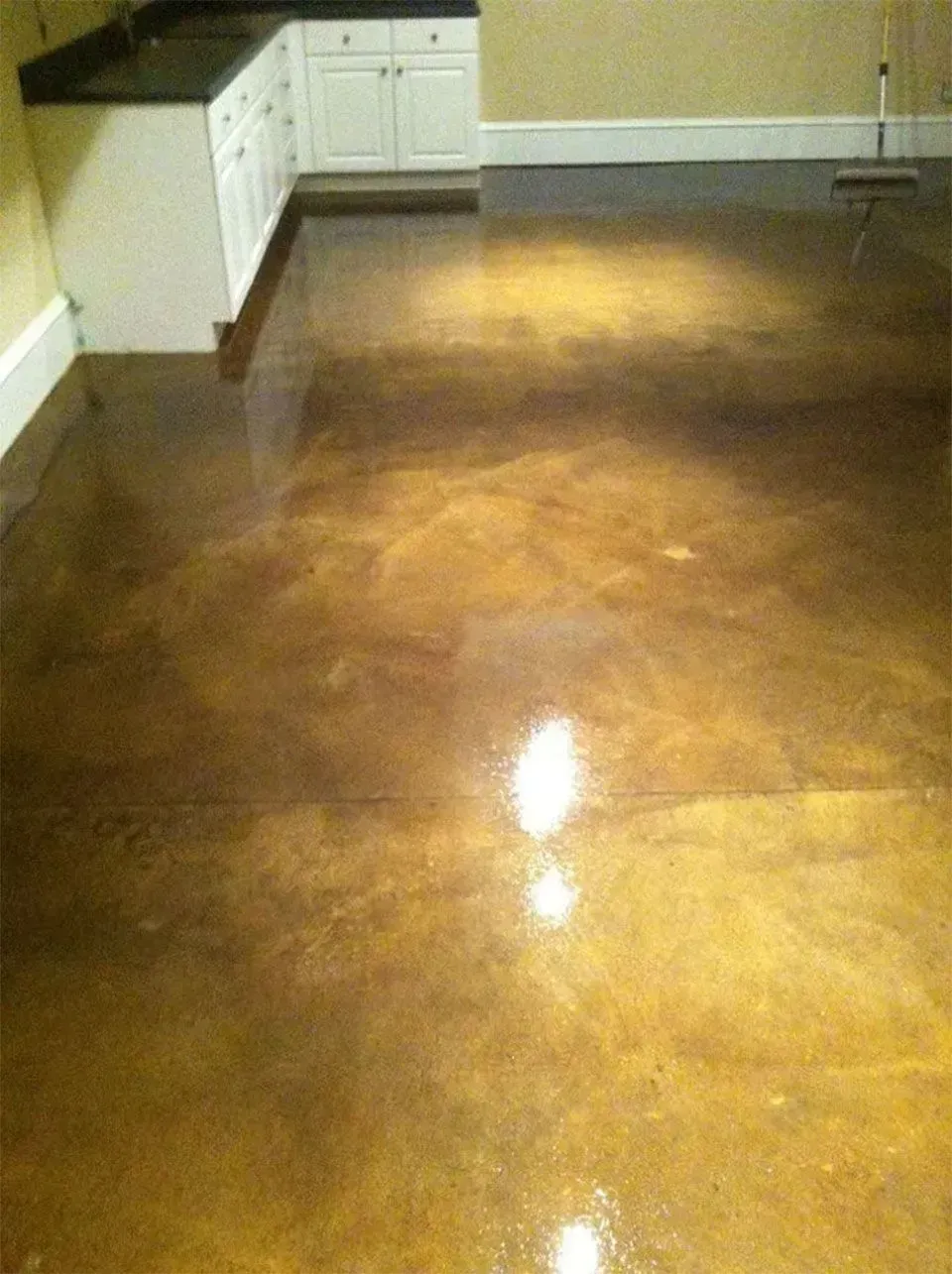 Golden-toned, polished concrete floor reflecting light. White cabinets and baseboards are in the corner of the room.