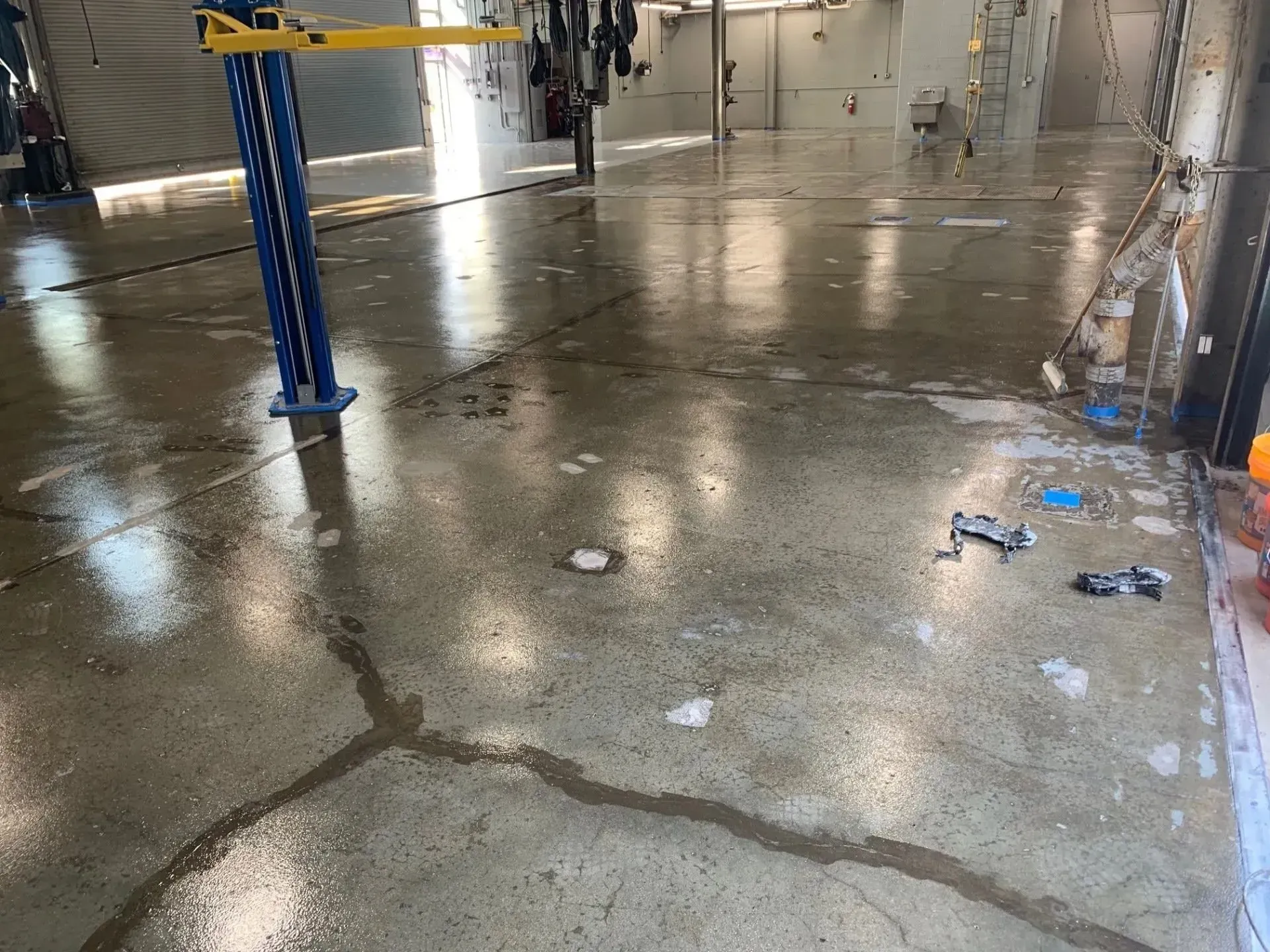 Wet concrete floor inside a garage with equipment visible. Cracks and puddles are present.