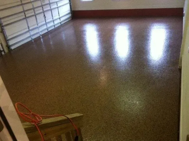 Garage floor with a speckled, glossy coating; light reflects from a partially open garage door and a window.