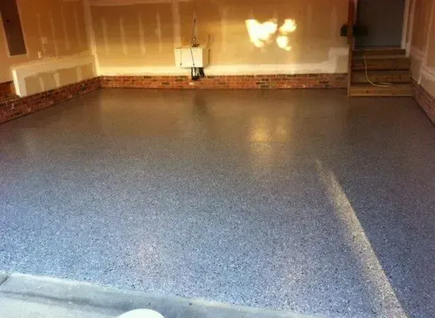 Garage floor coated with speckled blue-gray epoxy, with brick-like baseboards and bare walls.