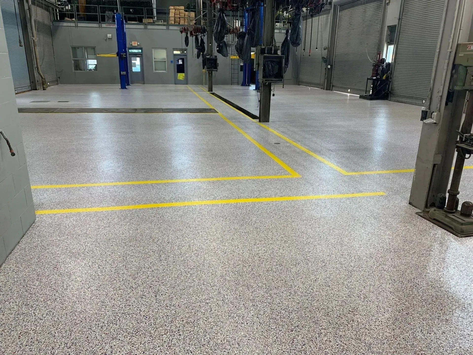 A brightly lit automotive repair shop interior with speckled floor and yellow lines.