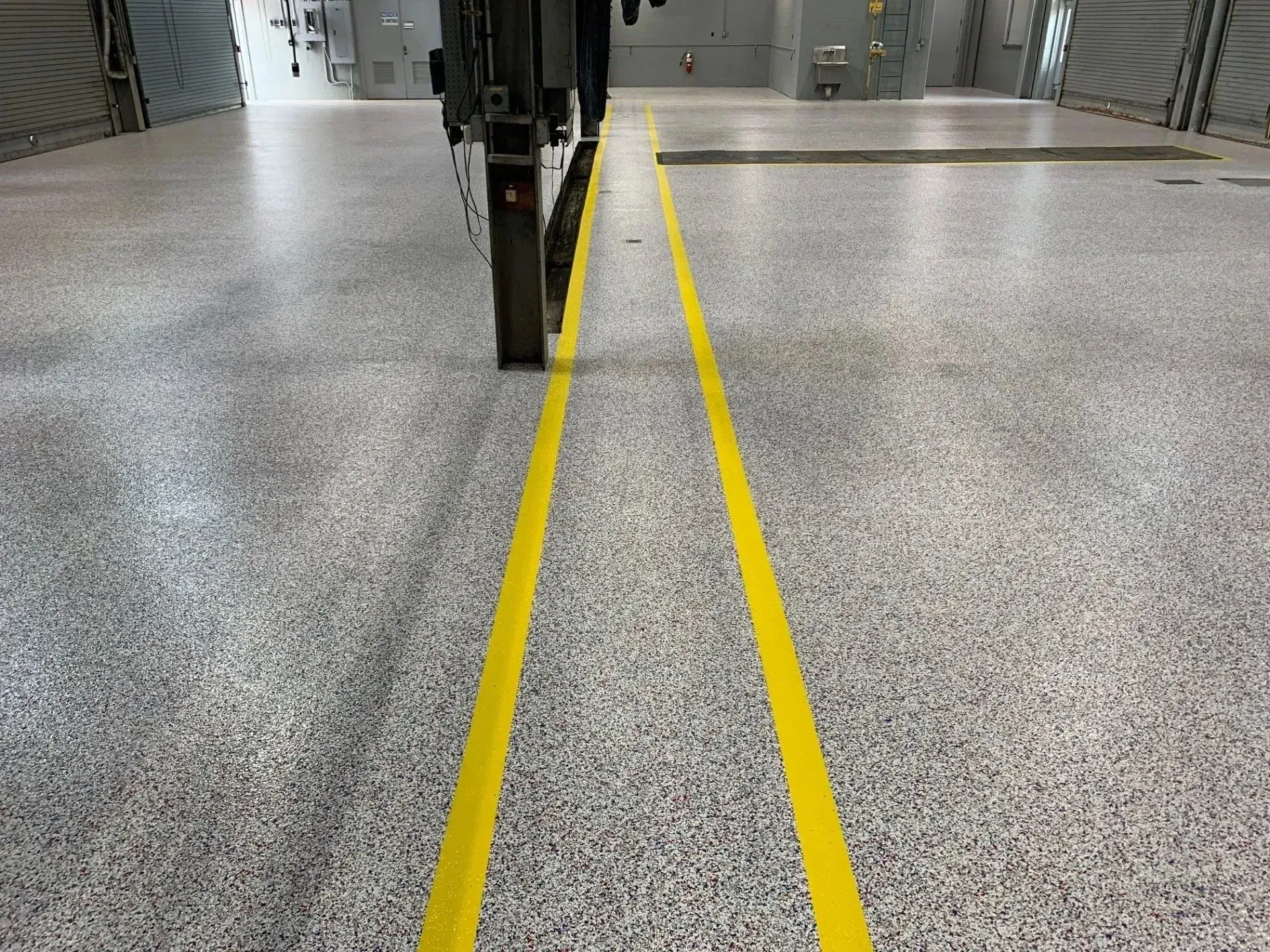 Yellow lines on speckled floor in industrial setting. A machine or equipment is visible.