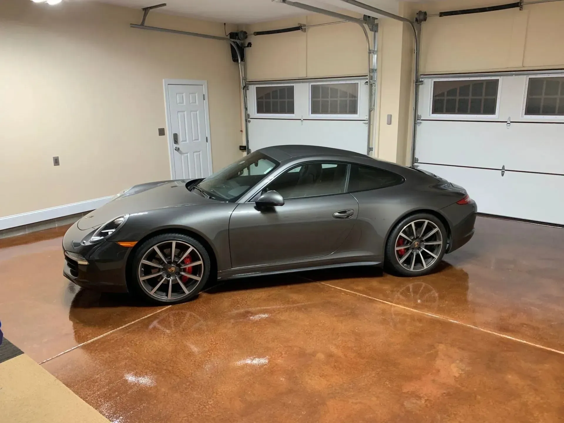 Dark gray Porsche 911 coupe parked in a well-lit garage with a decorative floor and closed garage doors.