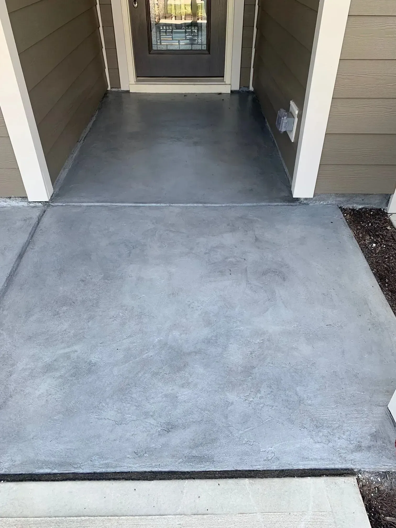 Gray concrete entryway with a front door and brown siding.