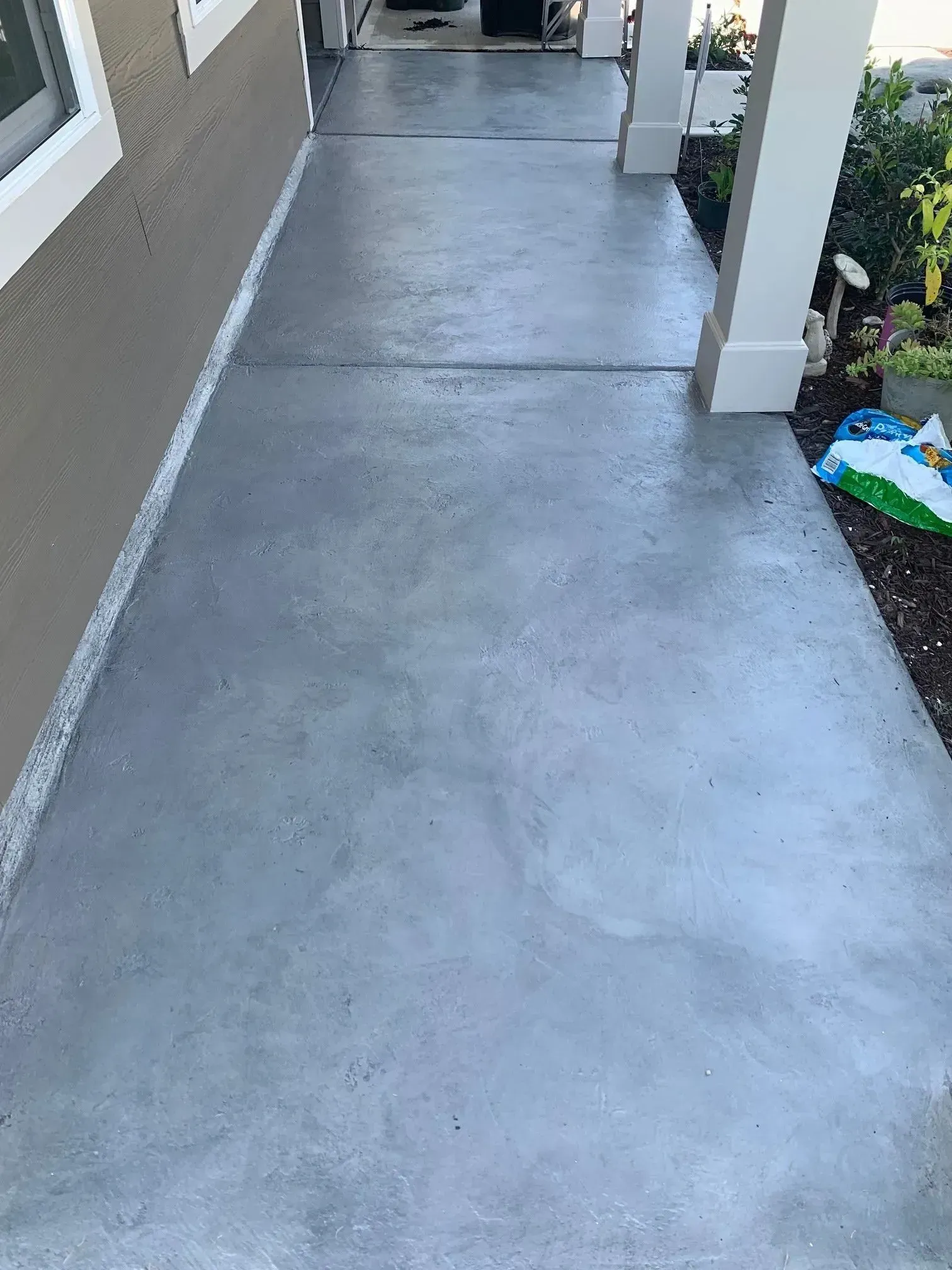 Gray concrete walkway alongside a beige building with white trim and a support column.
