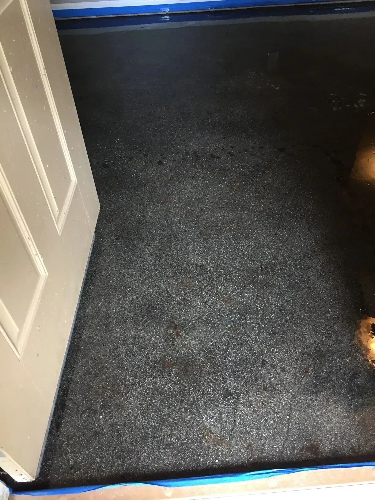 Gray speckled epoxy floor with a white door and blue painter's tape.