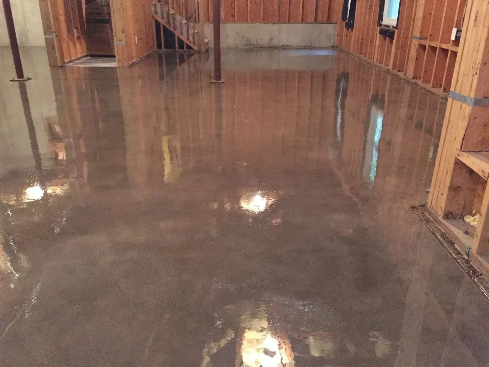 Brown, polished concrete basement floor reflecting light; wooden framing visible.