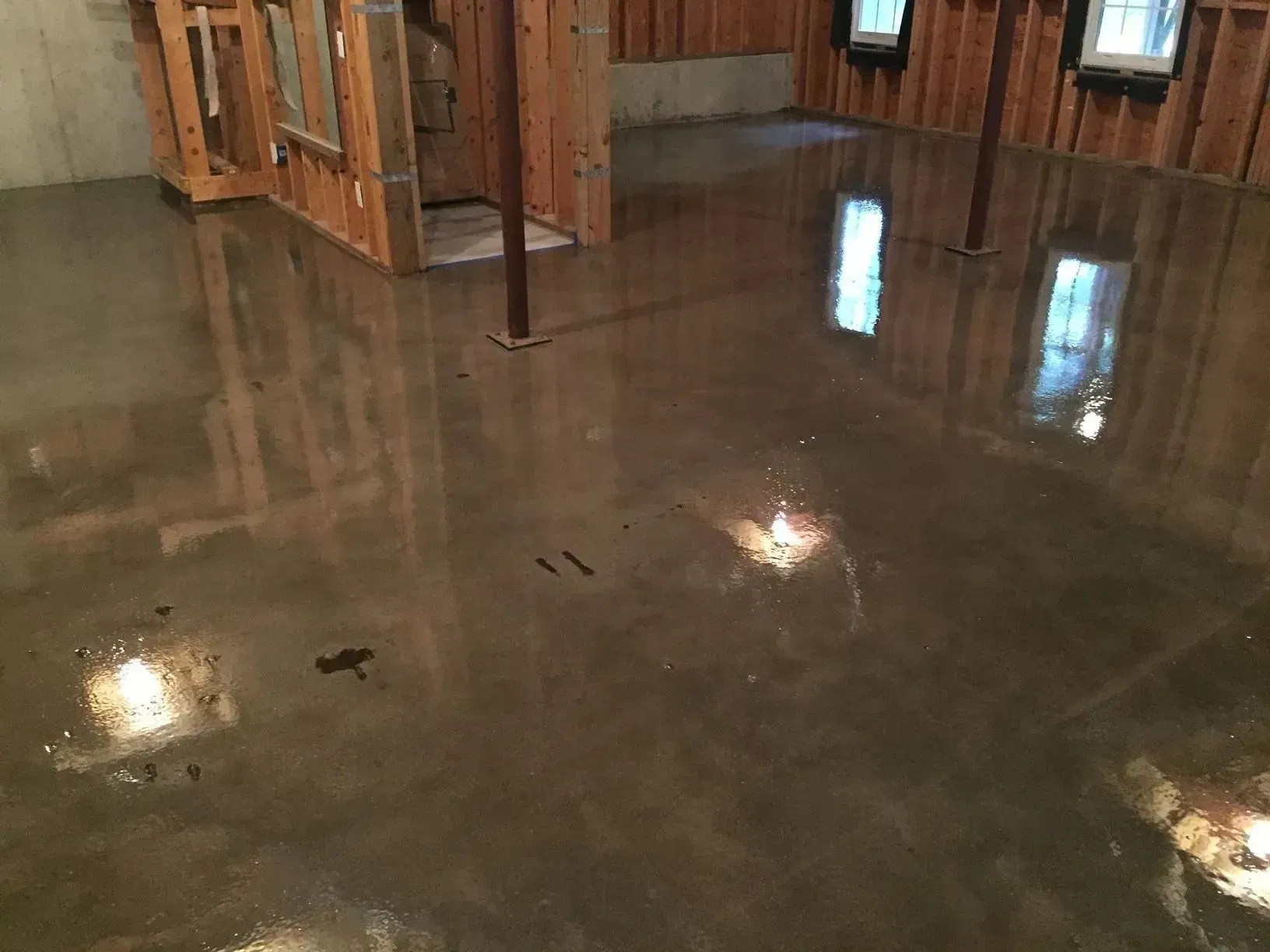 Glossy, dark-colored concrete floor in a room with wood-paneled walls and support beams. Reflections present.