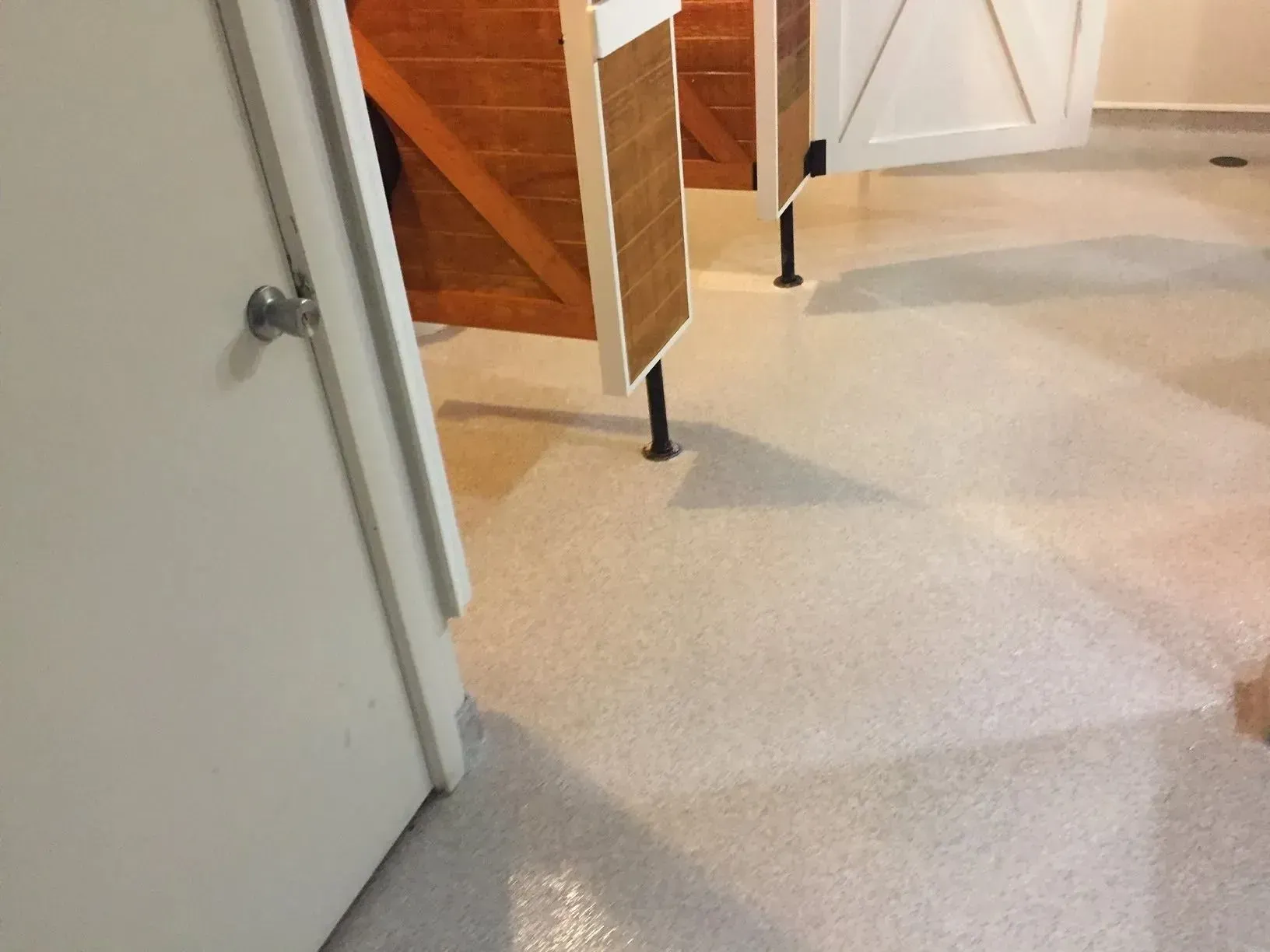 White and tan restroom with stalls. White doors, tan wall panels, and light floor.