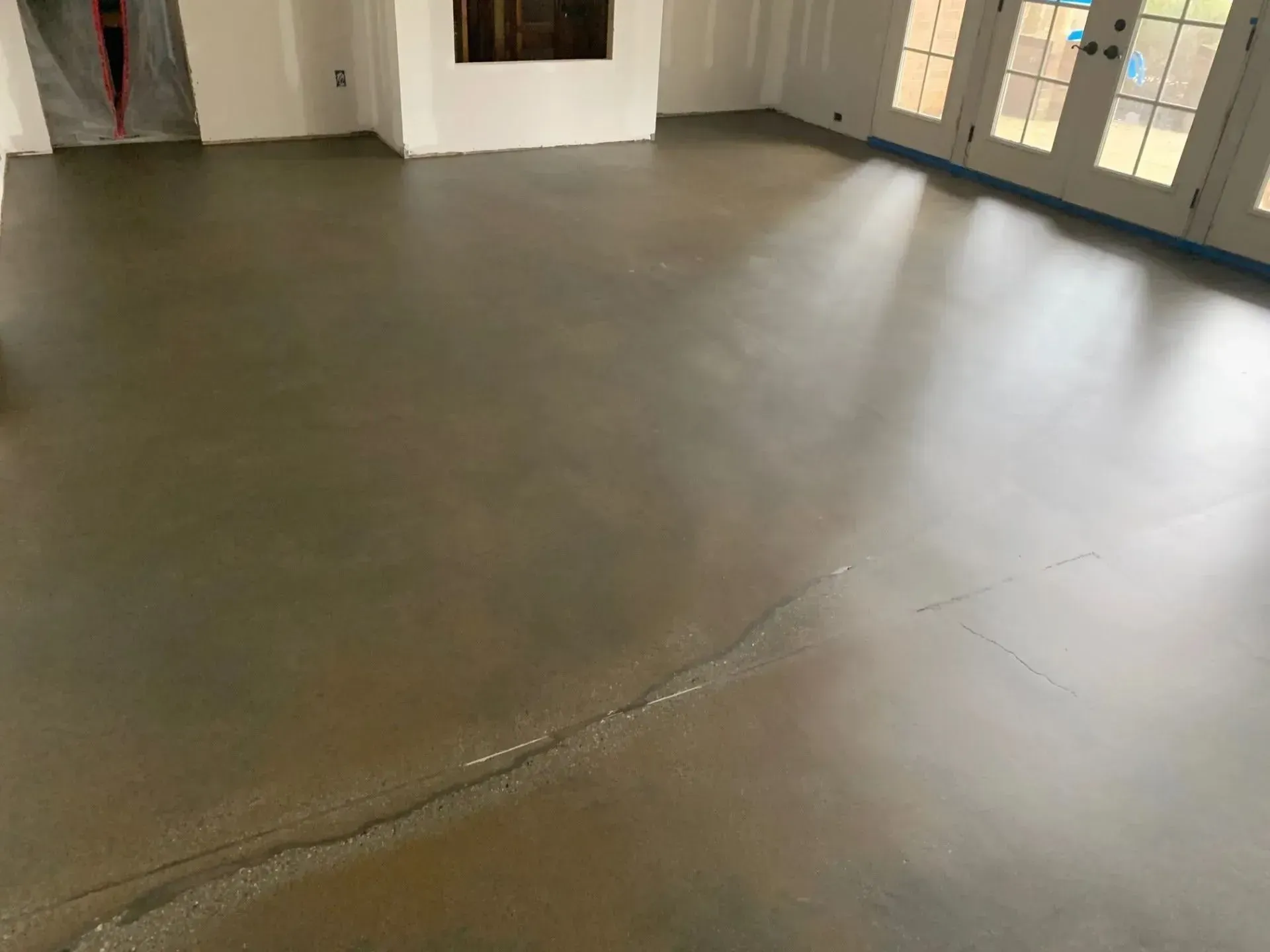 Polished concrete floor in a room with French doors. It has a slight sheen and a crack is visible.