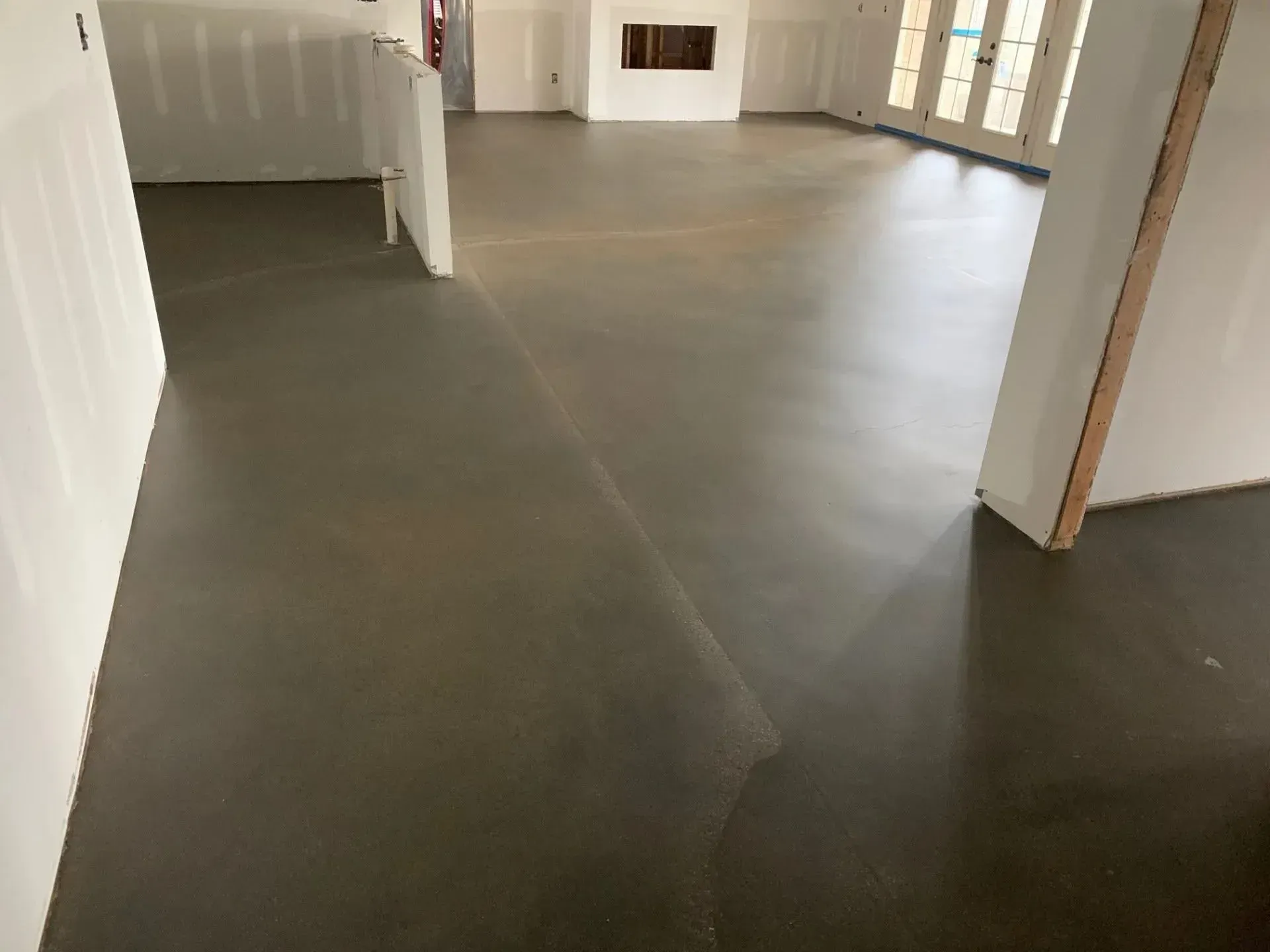 Dark gray concrete floor in a room under construction, with white walls and doorways.