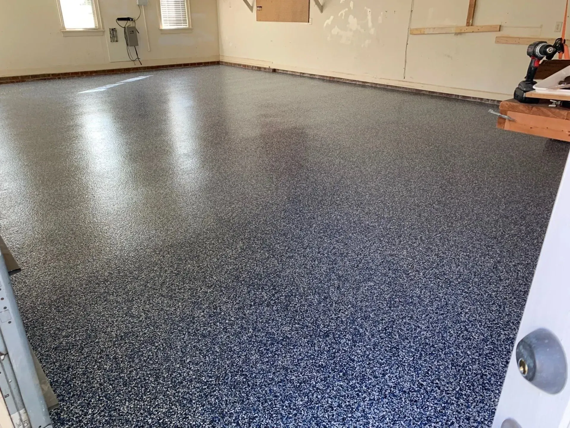 A garage with a shiny, speckled epoxy floor. Walls are off-white. Sunlight streams through a window.