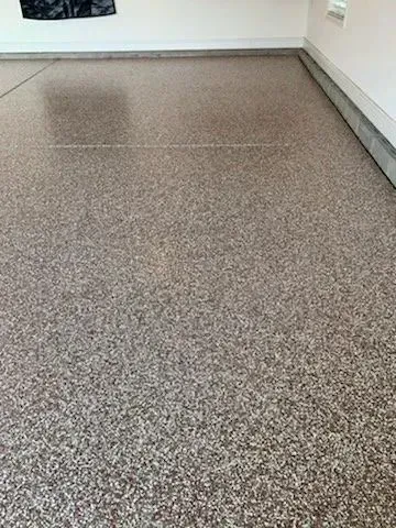 Speckled garage floor with light and dark brown tones, next to white wall.