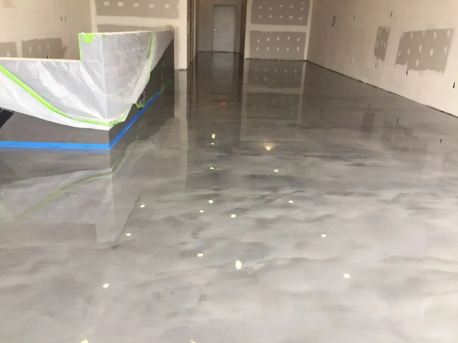 Shiny gray epoxy floor reflecting lights in a construction space, with a counter covered in plastic wrap.