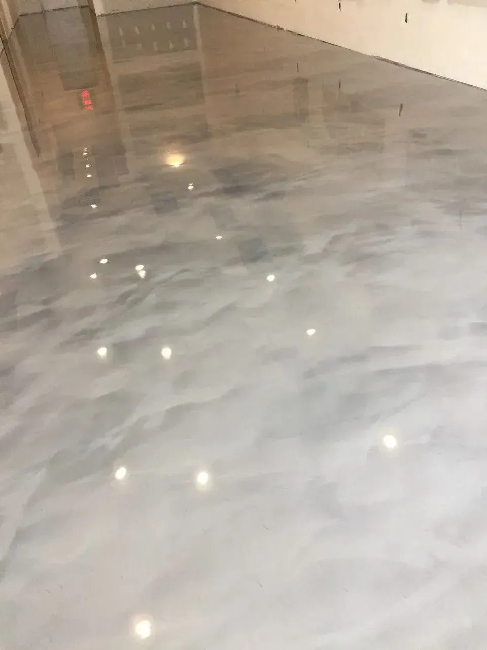 Metallic epoxy floor, shiny, reflective, light gray and white swirls, indoors.