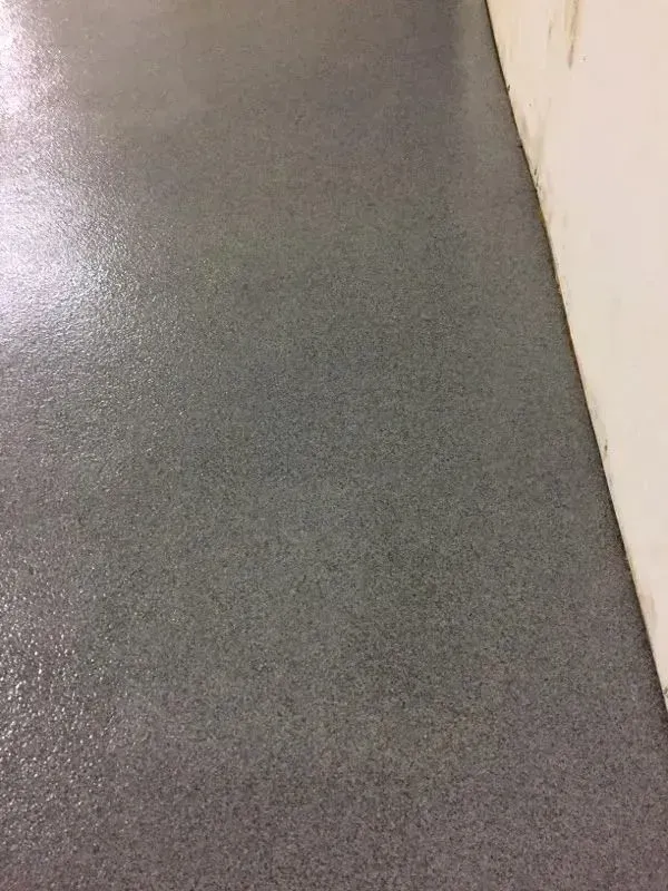 Gray, textured floor surface next to a white wall.