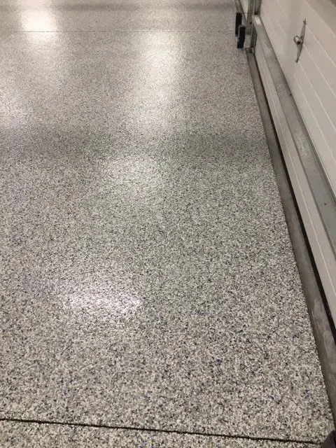 Gray speckled epoxy garage floor next to a white garage door.