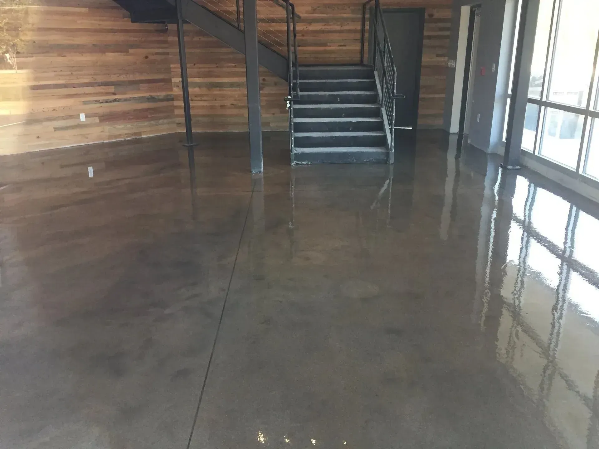 Interior view of a modern building with a shiny, dark floor and a metal staircase. Wooden paneling on the wall.