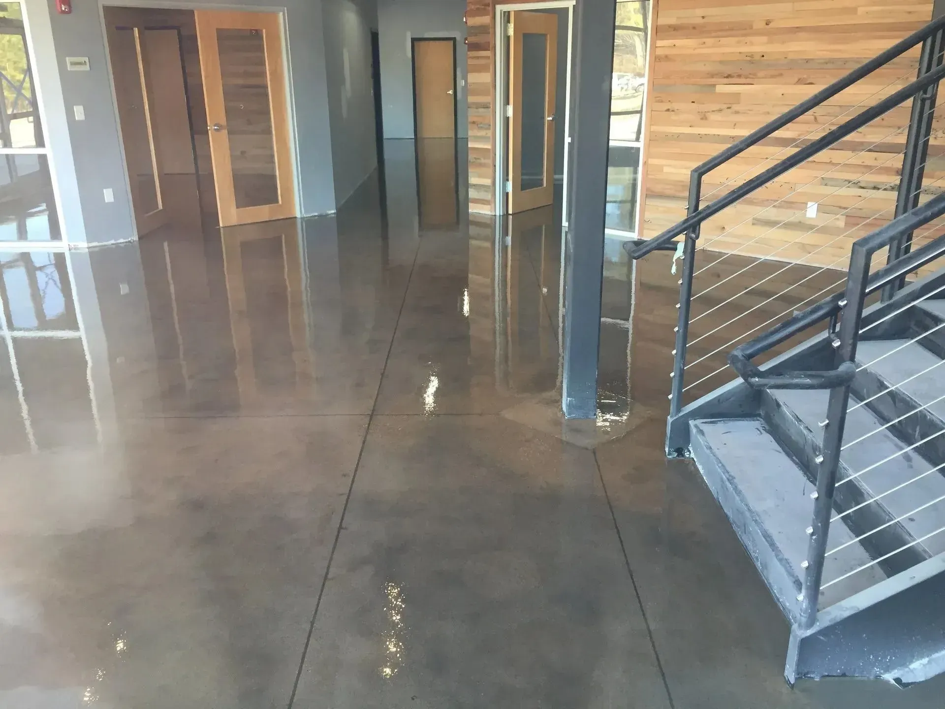 Polished concrete floor in a building interior, with wooden doors and a metal staircase.