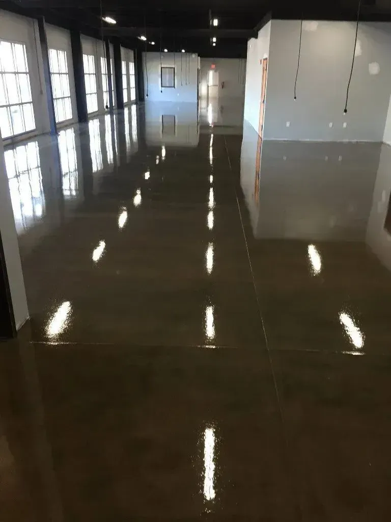 Shiny, reflective brown floor in a large, empty room with white walls and windows.