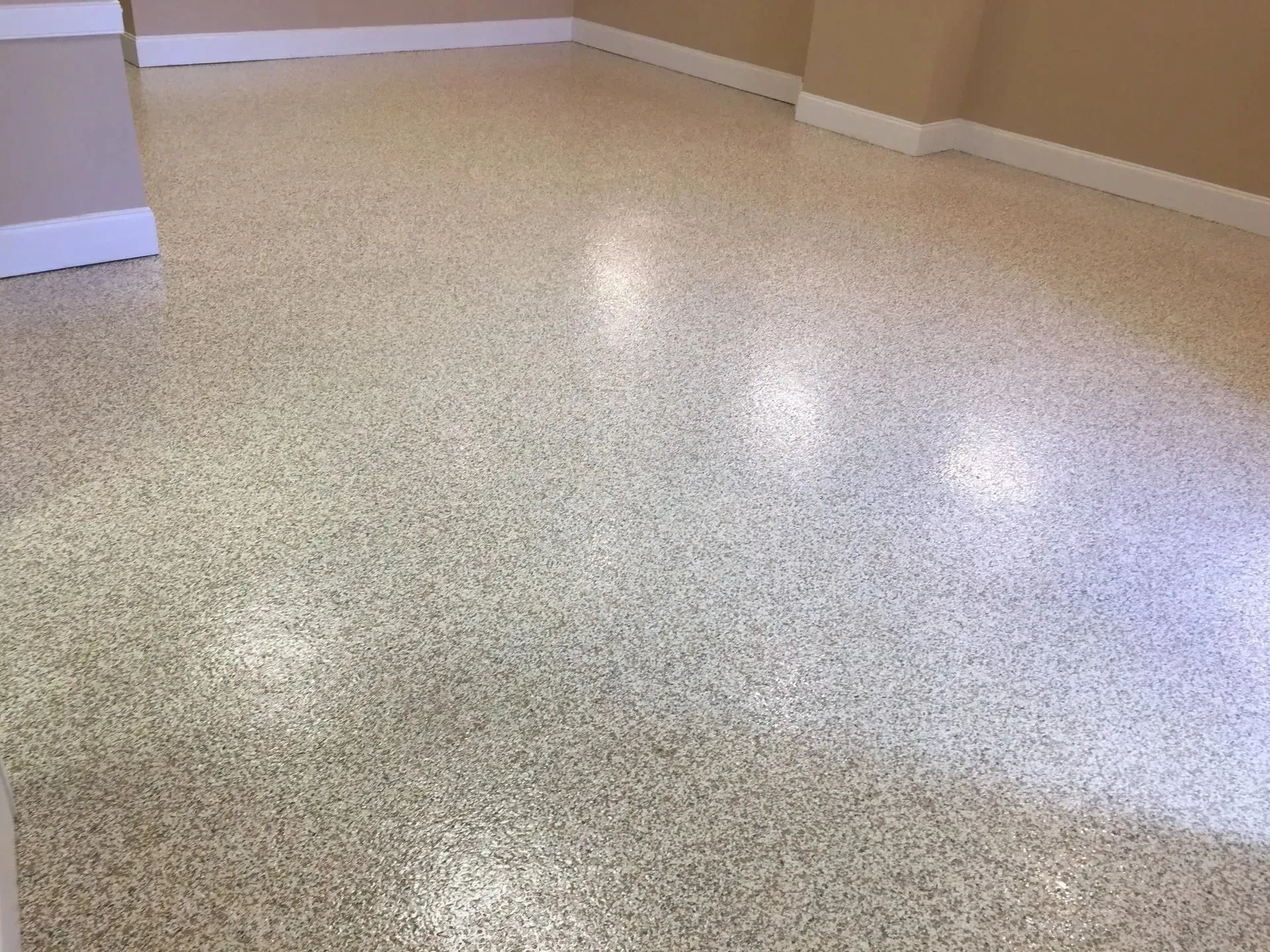Tan speckled epoxy floor in a room, with white baseboards and neutral walls.