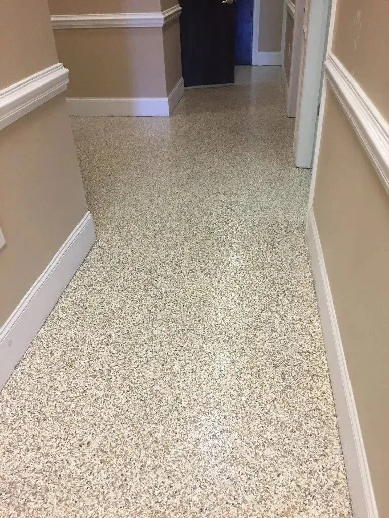Hallway with speckled flooring, tan walls, and white trim.
