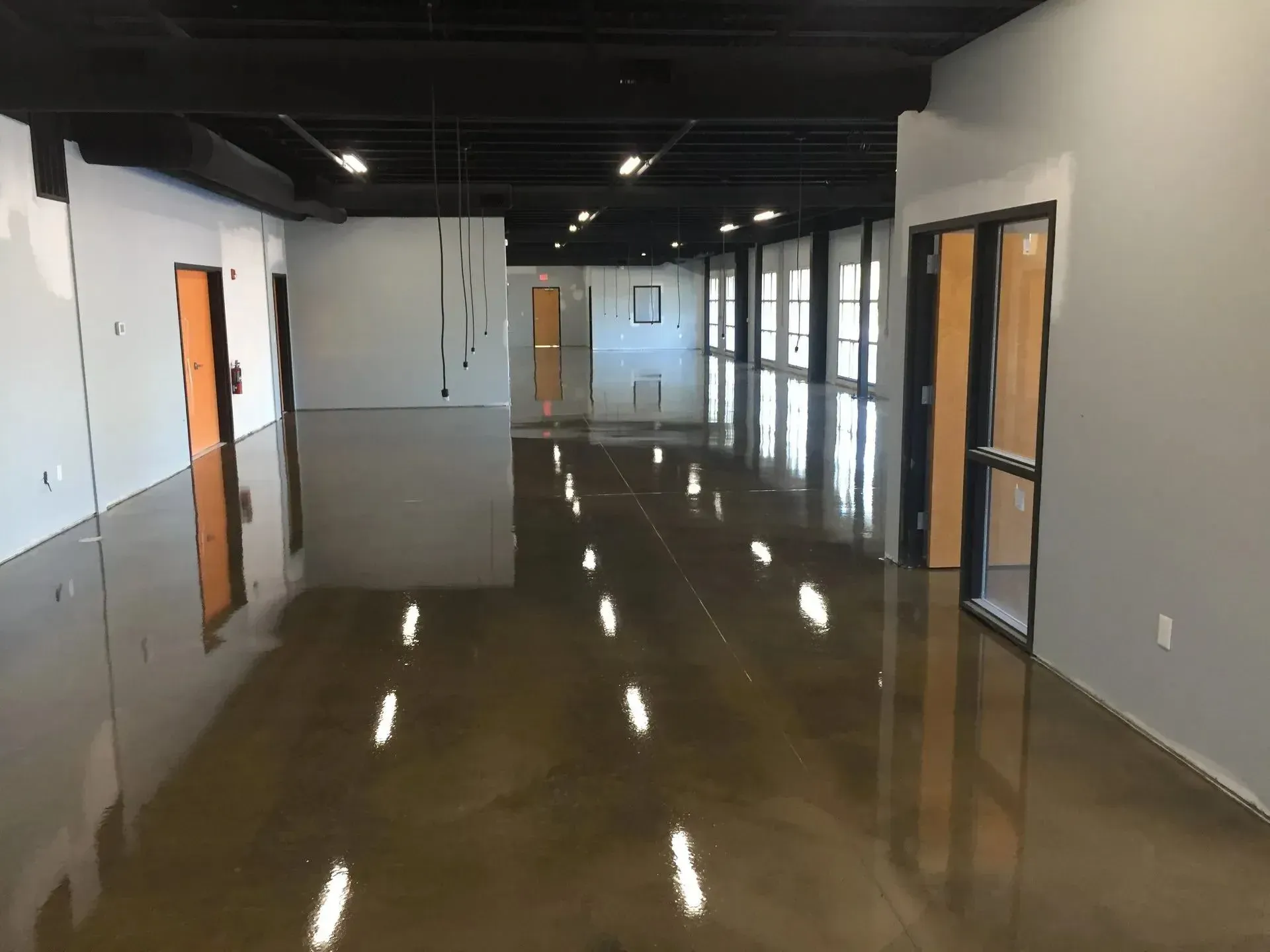 Empty office space with polished concrete floor, orange doors, and black ceiling.