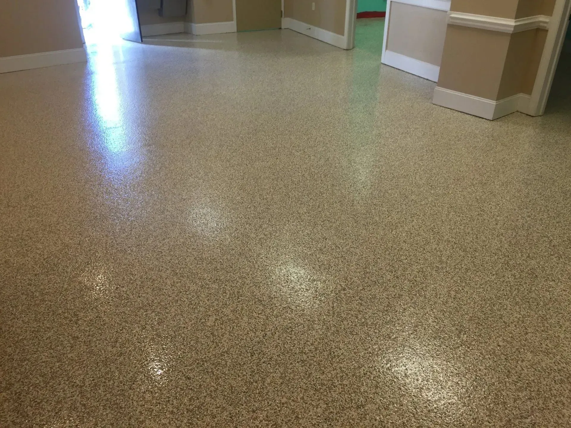 Beige speckled epoxy floor, reflecting light, in a room with doorways and cream-colored walls.