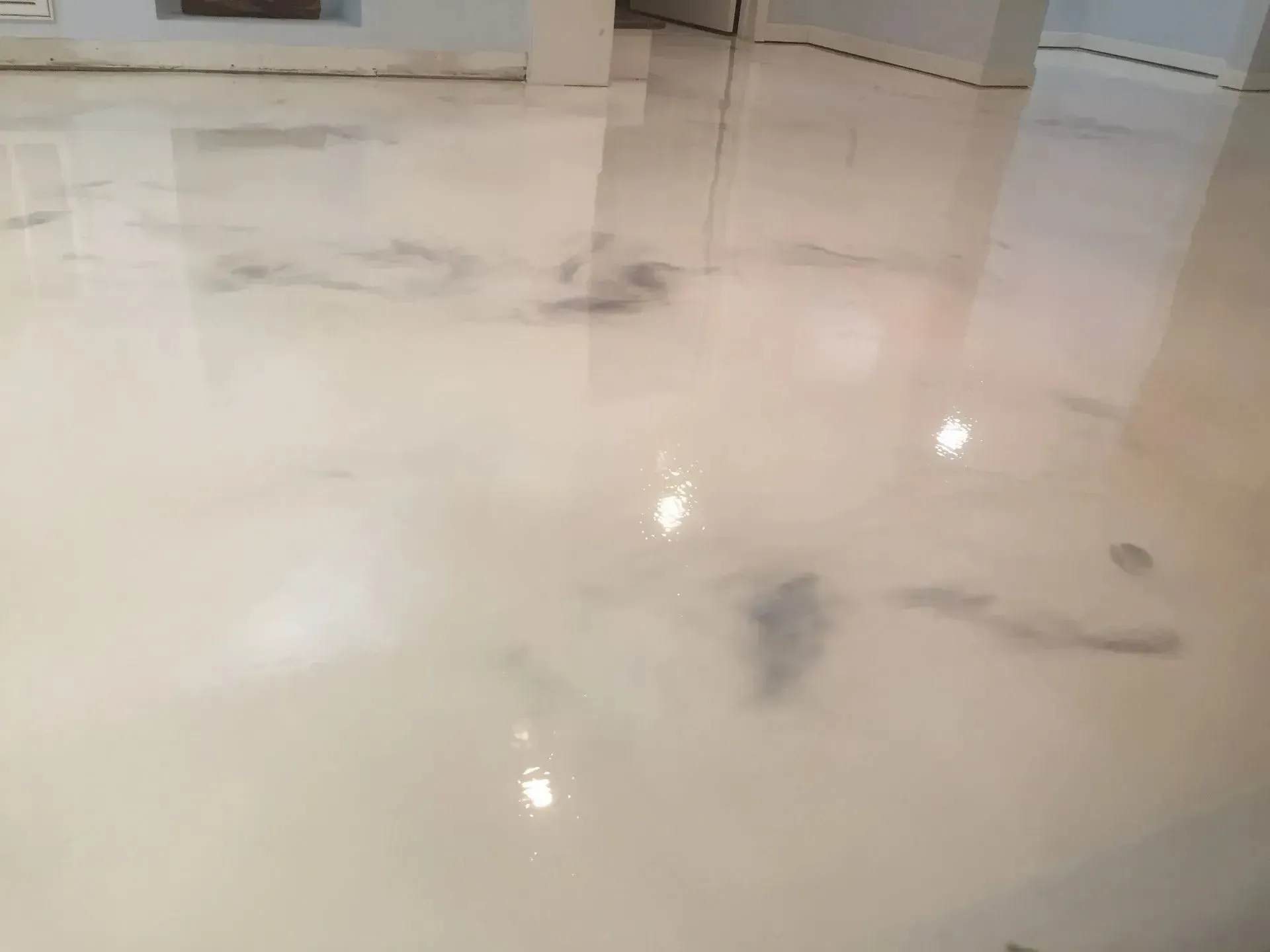 Shiny, light-colored epoxy flooring with dark gray marbling and light reflections in a room.