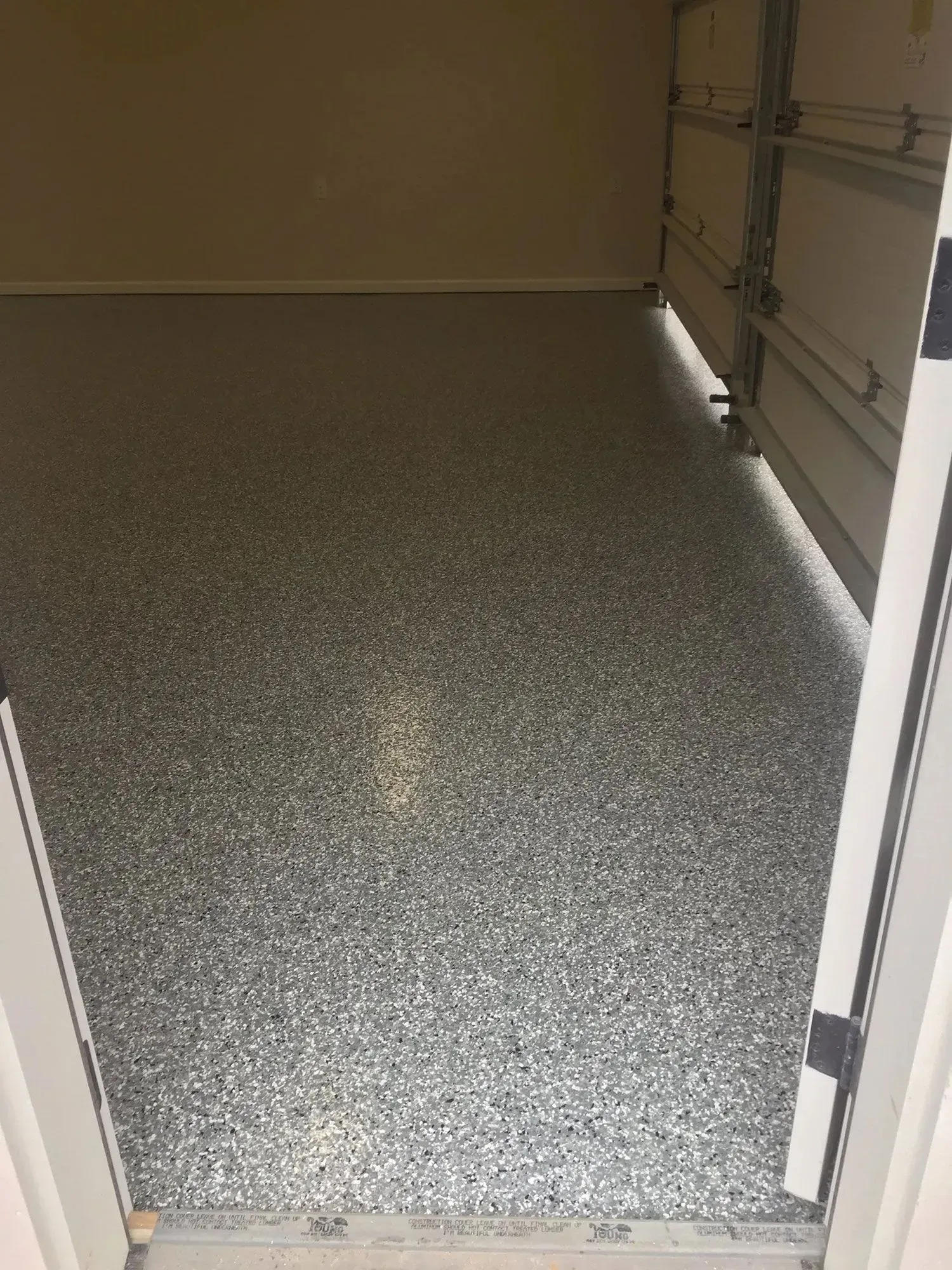 Garage interior with speckled gray floor and open garage door.