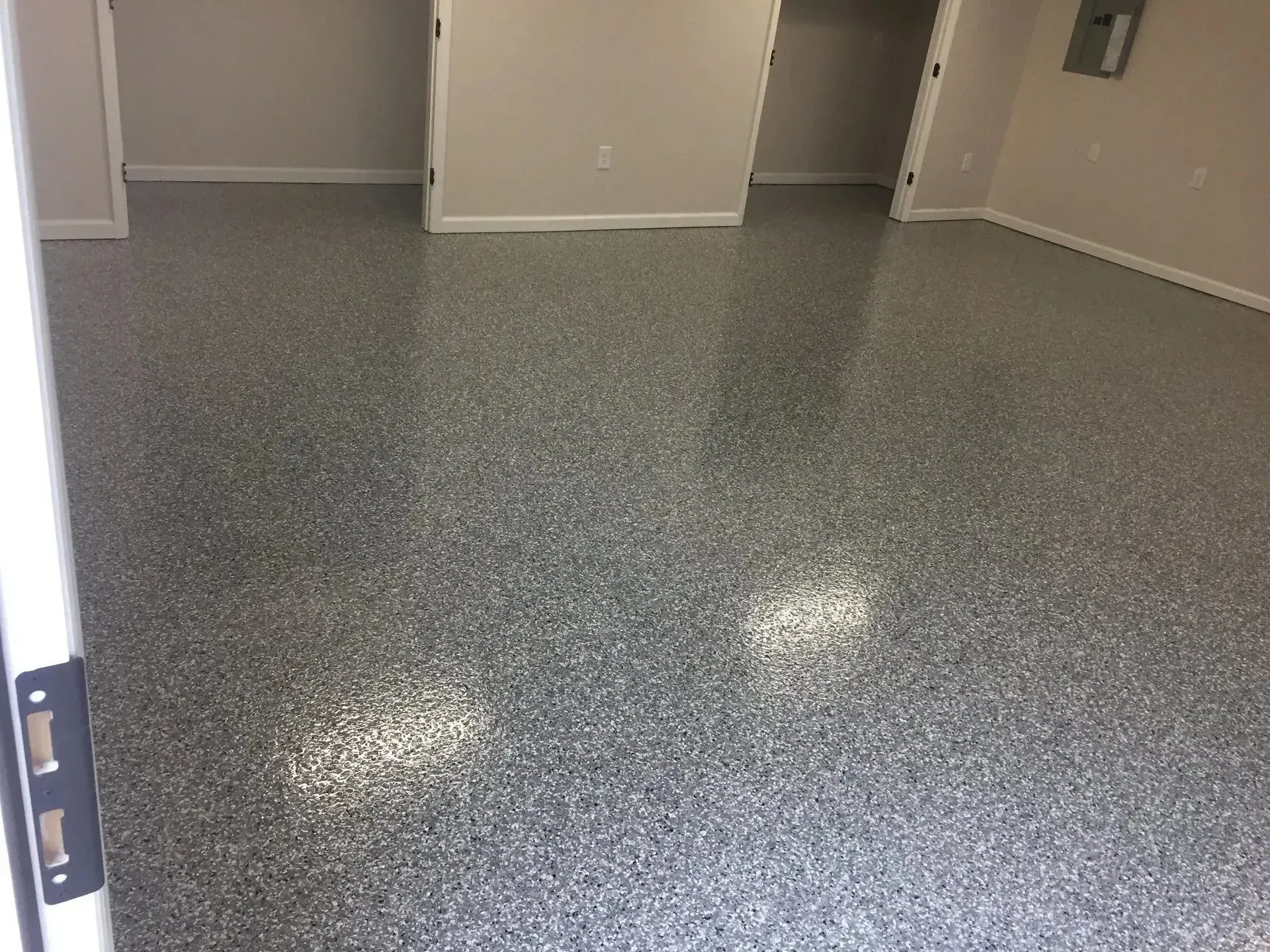 Gray speckled epoxy floor in a room, reflecting light. Open doorways, neutral walls.