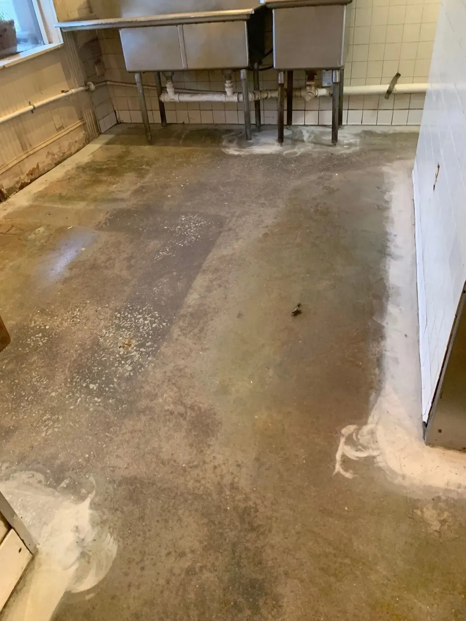 Concrete floor with white residue, commercial kitchen with metal cabinetry.
