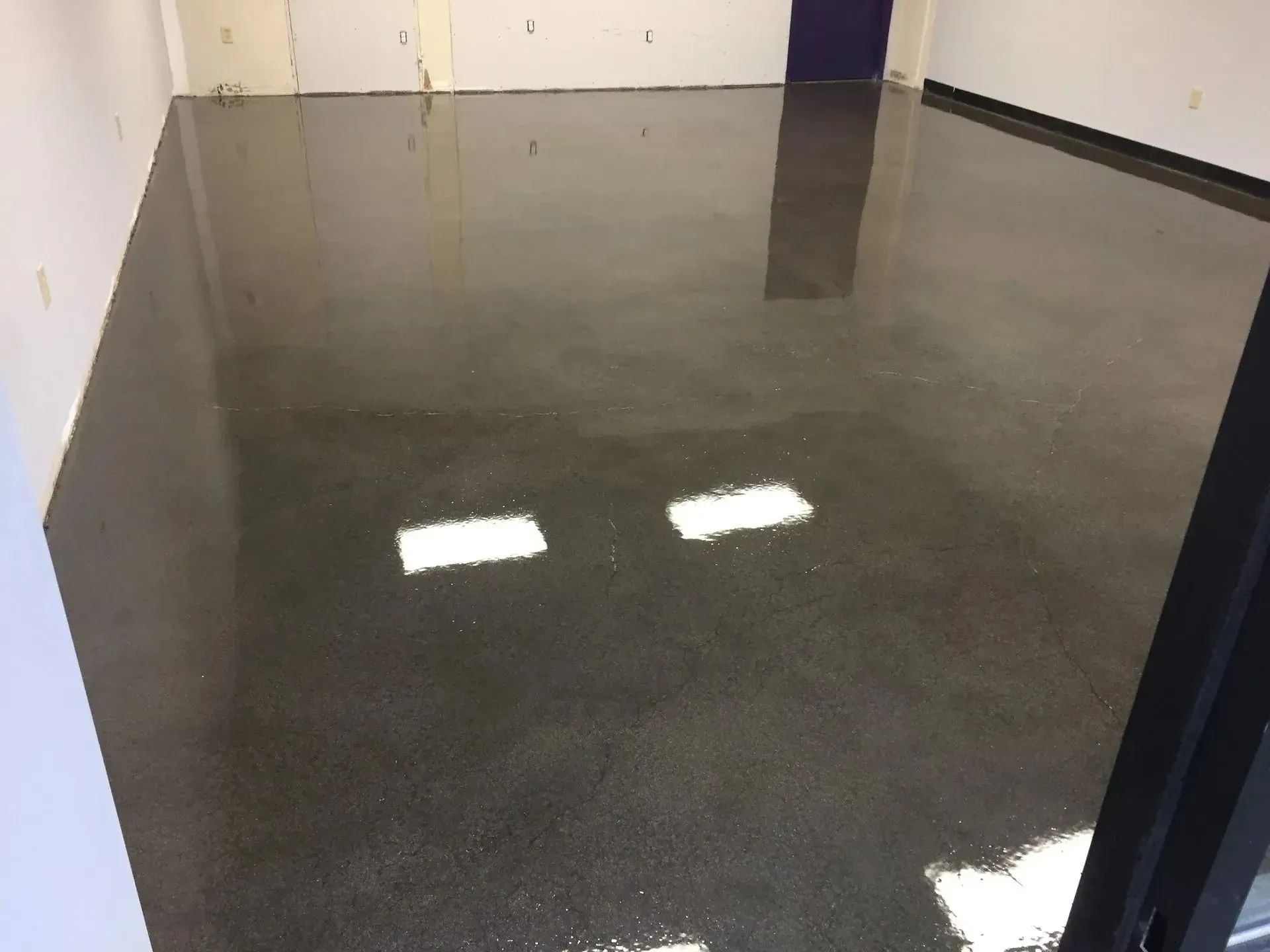A shiny, dark gray concrete floor in an empty room, reflecting overhead lights.