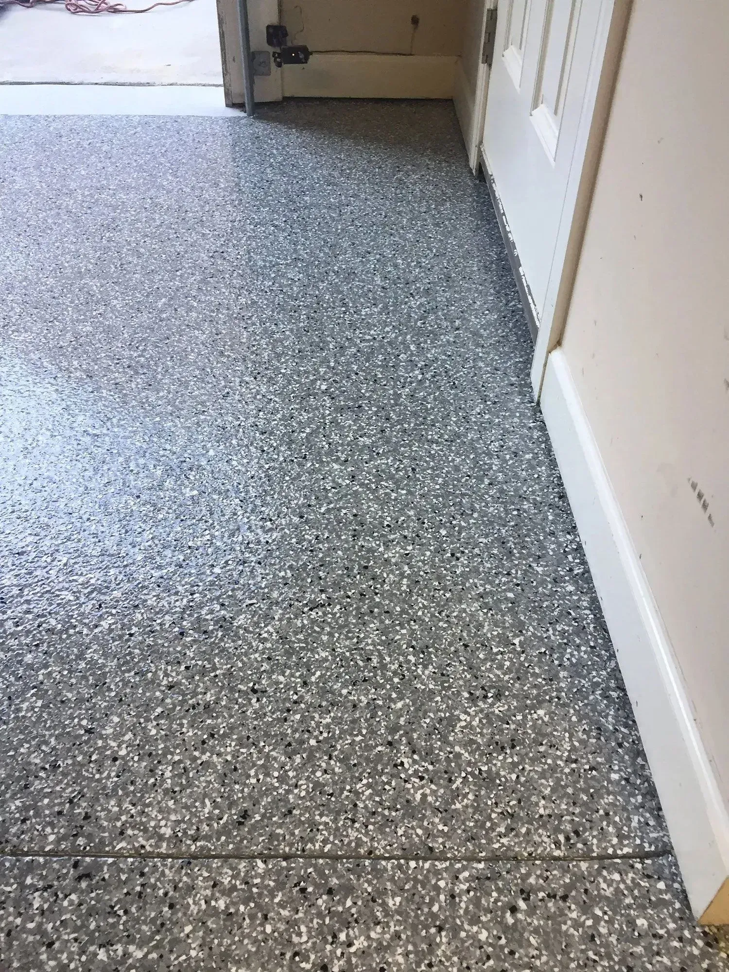 Gray speckled epoxy garage floor next to a white door frame and baseboard.